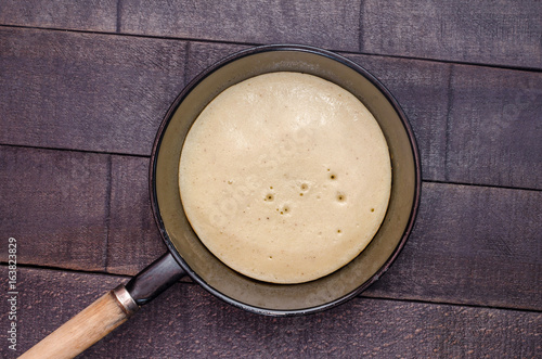 Raw pancake in a frying pan on a dark background