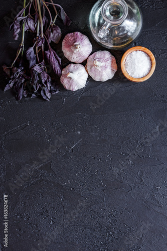 Cook workplace. Garlic, basil on black table background top view copyspace