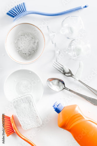 Dishwashing liquid, sponge, brush and tableware on white background top view