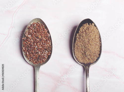 Whole flaxseed and ground flaxseed on two old vintage spoons on pink marble background. Flat lay. Top view 