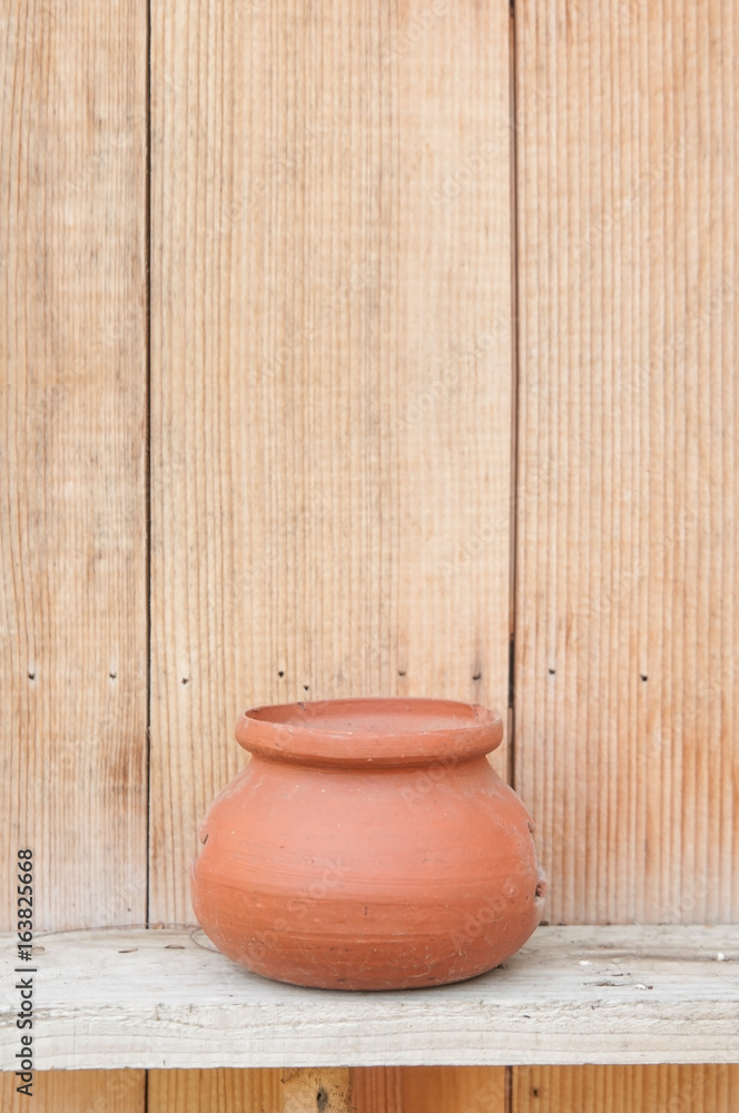 Small clay plant pot on wooden shelf with wood background. Small clay plant pot on wooden shelf with wood background.