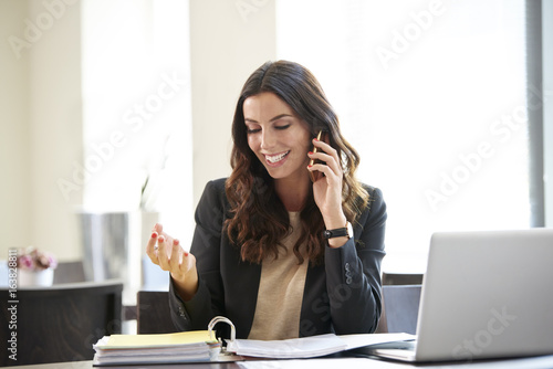 Keep in touch with clients. Shot of a young businesswoman sitting at office desk in front of laptop and making call while onsidering the possibilities with her client.