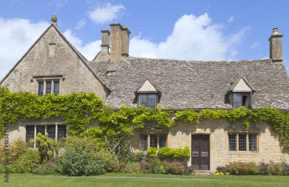 Charming old stone house with climbing wisteria on the wall and flowers, shrubs in the front garden, on a sunny summer day .