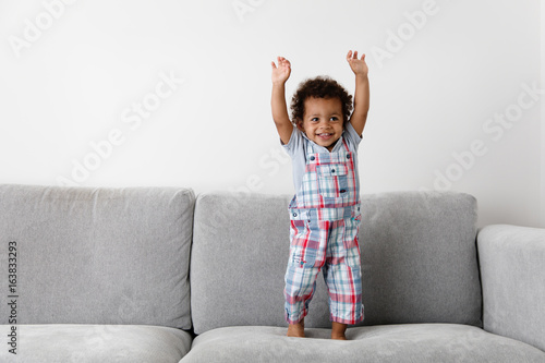 smiling toddler standing on couch with hands up photo