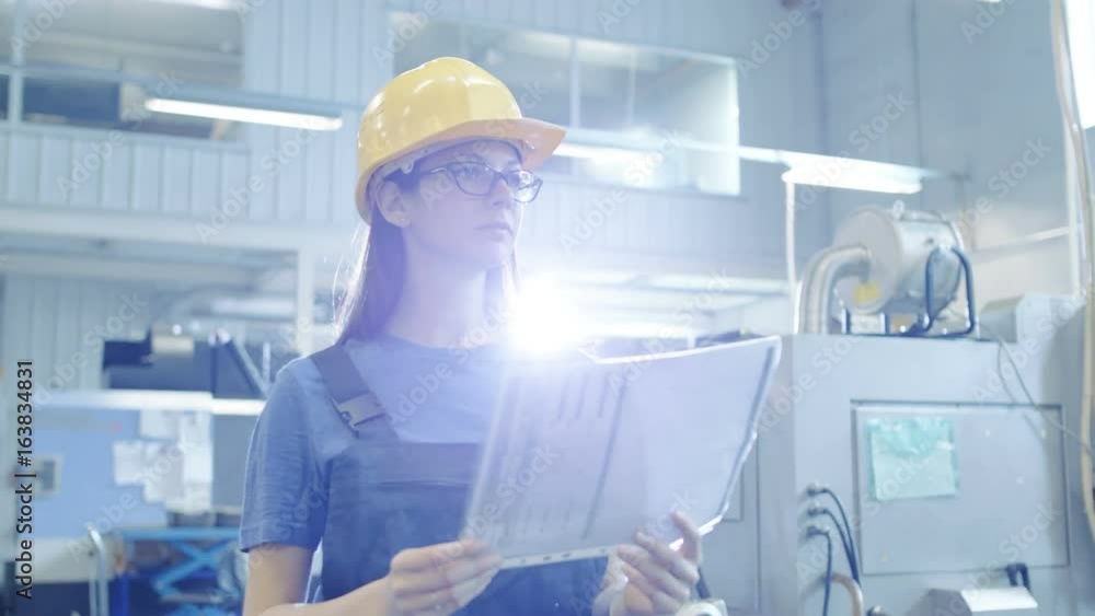 Beautiful Female Industrial Worker Walks and Reads Documents in Big Factory Building.Shot on RED EPIC-W 8K Helium Cinema Camera. Beautiful Female Industrial Worker Walks and Reads Documents in Big Factory Building.Shot on RED EPIC-W 8K Helium Cinema Camera.