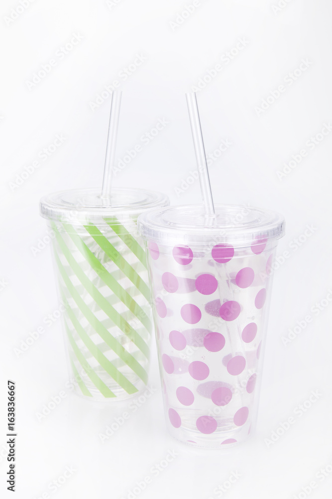 Green and pink plastic tumblers on a white surface. Tumblers isolated on white background. Green and pink plastic tumblers on a white surface. Tumblers isolated on white background.