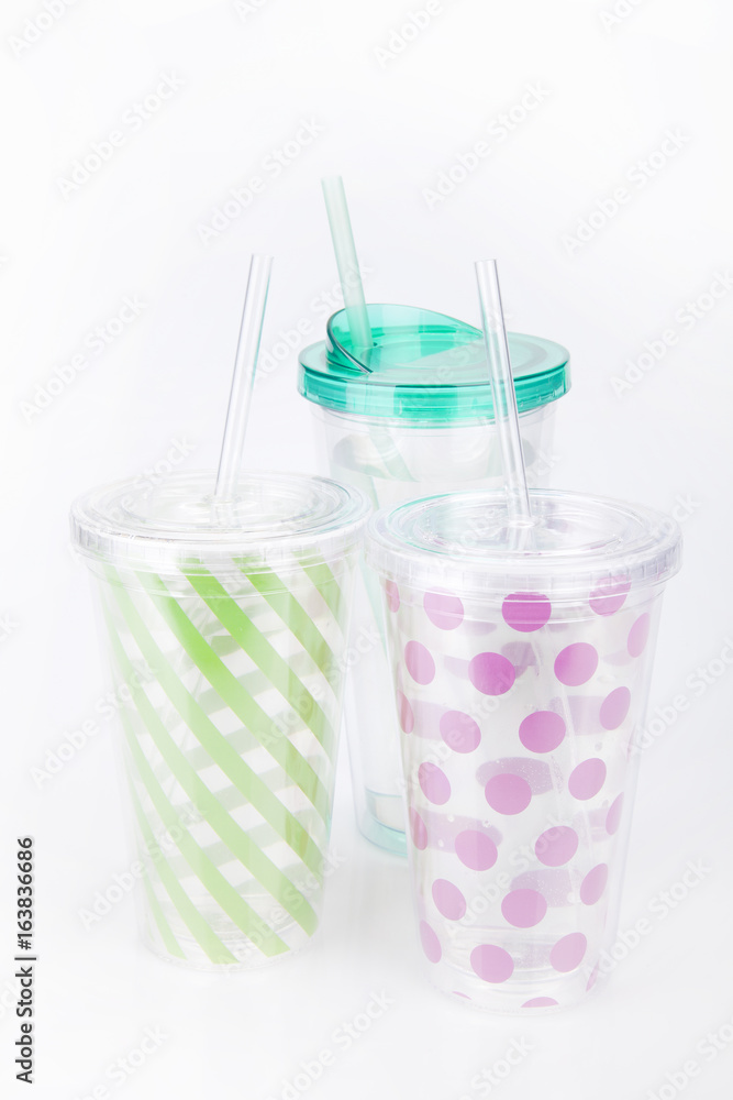 Green and pink plastic tumblers on a white surface. Tumblers isolated on white background. Green and pink plastic tumblers on a white surface. Tumblers isolated on white background.