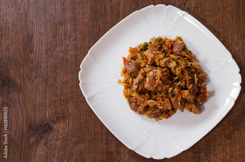 Rice with meat and vegetables in a plateon the brown wooden table background. rustic kitchen table with copy space. top view.