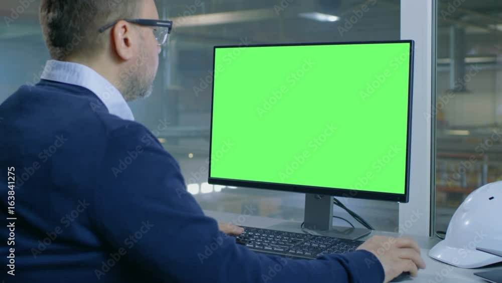 Chief Engineer Works on His Computer with Mock-up Green Screen. Inside of the Factory is Seen From Her Office Window.Shot on RED EPIC-W 8K Helium Cinema Camera. Chief Engineer Works on His Computer with Mock-up Green Screen. Inside of the Factory is Seen From Her Office Window.Shot on RED EPIC-W 8K Helium Cinema Camera.