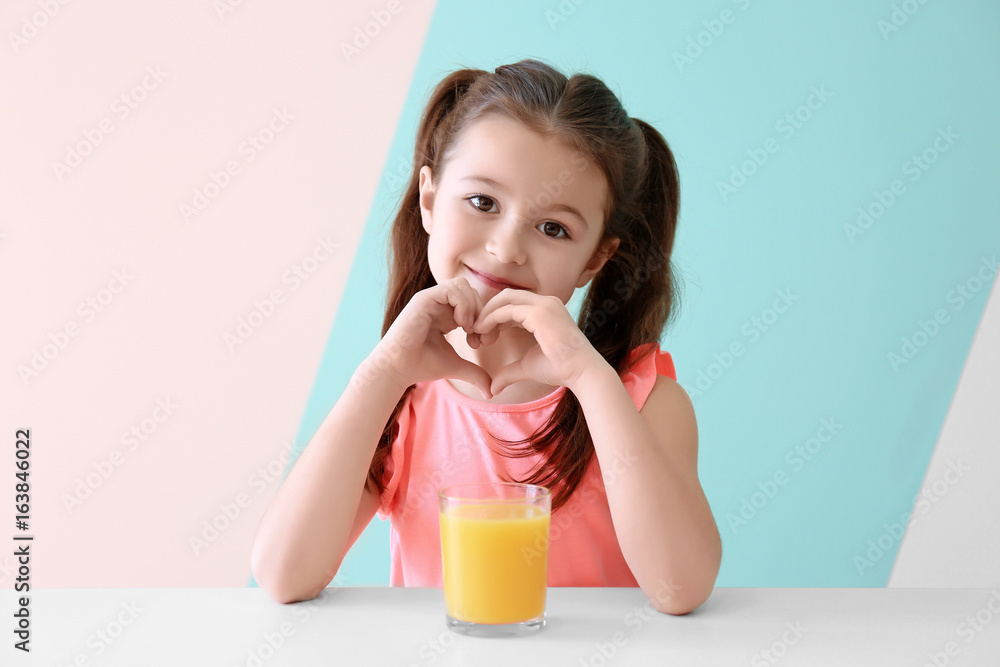 Cute little girl with glass of juice sitting at table, on color background Cute little girl with glass of juice sitting at table, on color background