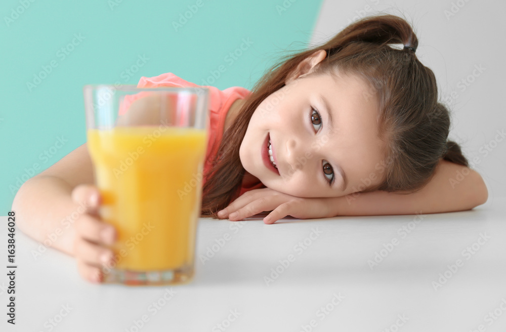 Cute little girl with glass of juice sitting at table, on color background Cute little girl with glass of juice sitting at table, on color background