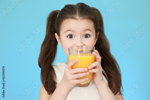 Cute little girl drinking juice on color background