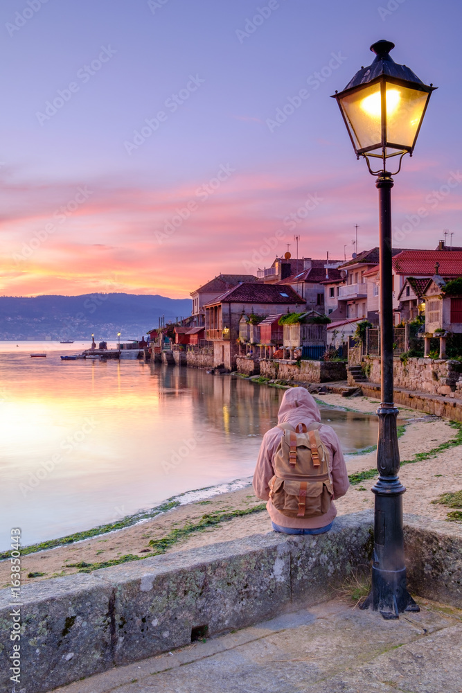 tourist sitting on his back at sunrise in the town of Combarro, Pontevedra, Galicia, Spain