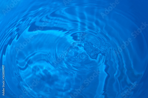 Texture of a drop falling into the blue water, close-up