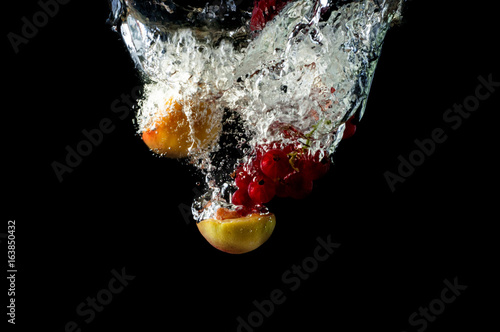 A falling fresh fruits and berries in water, a splash with bulbs on a black background