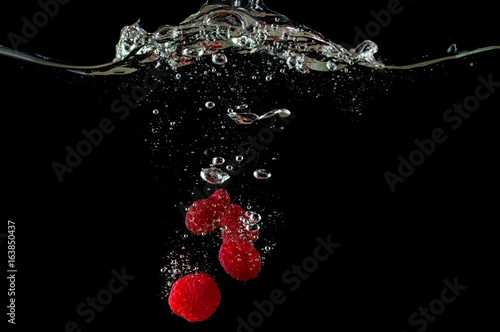 A falling fresh raspberry in water, a splash with bulbs on a black background