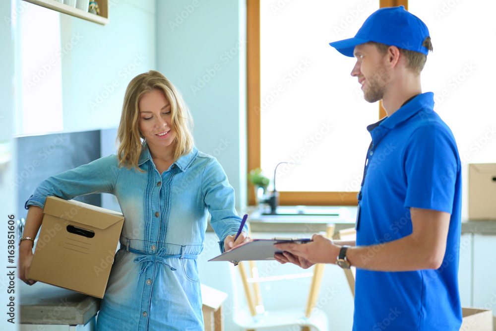 Smiling delivery man in blue uniform delivering parcel box to recipient - courier service concept Smiling delivery man in blue uniform delivering parcel box to recipient - courier service concept