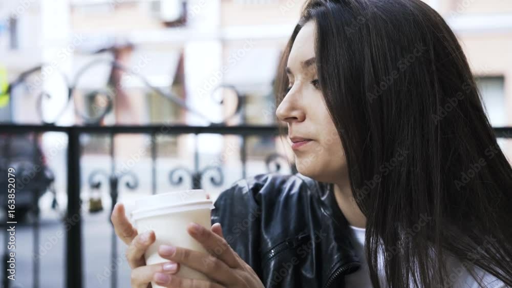 Close up of an attractive young woman drinking coffee from a paper cup sitting in a downtown cafe. Handheld real time close up shot Close up of an attractive young woman drinking coffee from a paper cup sitting in a downtown cafe. Handheld real time close up shot