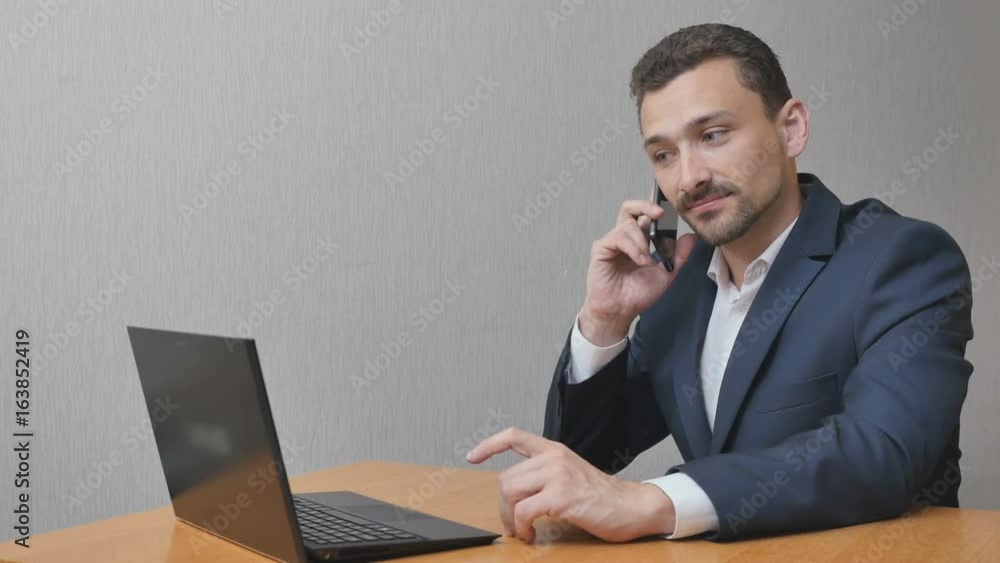 Businessman is finishing a heavy conversation on the phone. The man shakes his head in displeasure and sighs. A person works behind a laptop and has problems Businessman is finishing a heavy conversation on the phone. The man shakes his head in displeasure and sighs. A person works behind a laptop and has problems