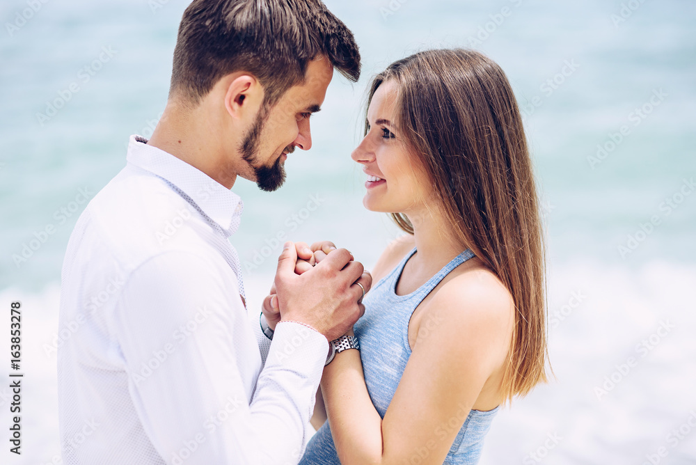 A beautiful pregnant woman in a blue dress and her courageous and handsome husband in a shirt and blue trousers leaned to each other against the background of the sea. A beautiful pregnant woman in a blue dress and her courageous and handsome husband in a shirt and blue trousers leaned to each other against the background of the sea.