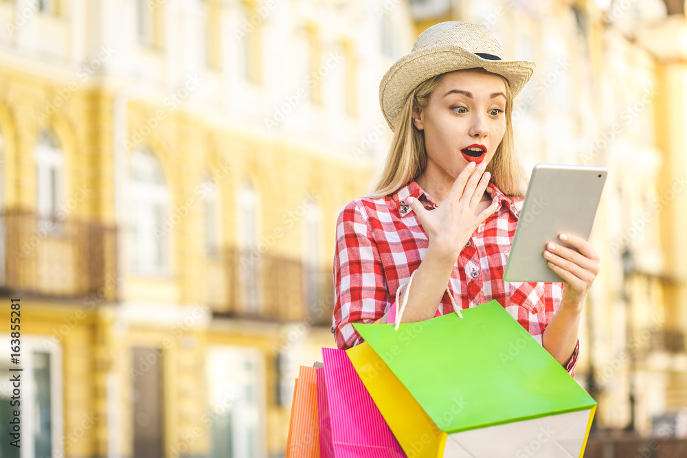 Obraz premium Portrait of young happy smiling woman with shopping bags. Online shopping. With tablet.