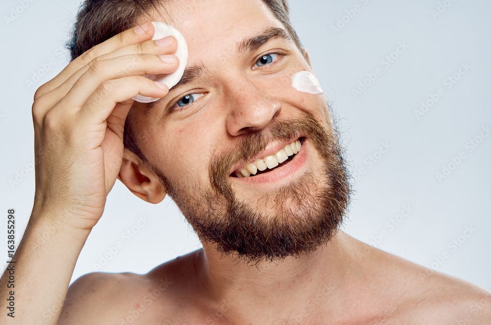 Obraz premium Young guy with a beard on a gray background, cotton ball, cream