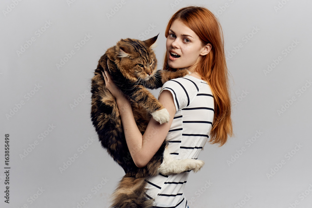 Beautiful young woman on a light background holds a cat