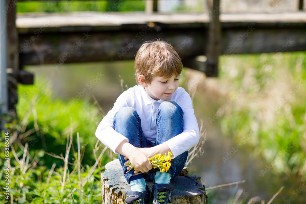 Little school kid boy sitting near river with flowers in hands. Little school kid boy sitting near river with flowers in hands.