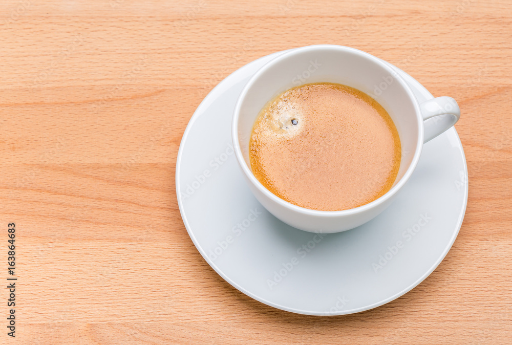 Hot black coffee with foam bubbles in white cup with wooden board in background, morning coffee concept. Hot black coffee with foam bubbles in white cup with wooden board in background, morning coffee concept.