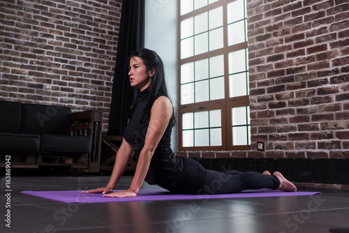 Female yoga beginner doing bhujangasana cobra pose on mat in loft apartment