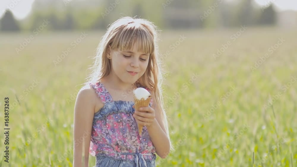 Beautiful blond little girl eats ice-cream in the summer against the background of a wheat field. Warm sunny day. Beautiful blond little girl eats ice-cream in the summer against the background of a wheat field. Warm sunny day.