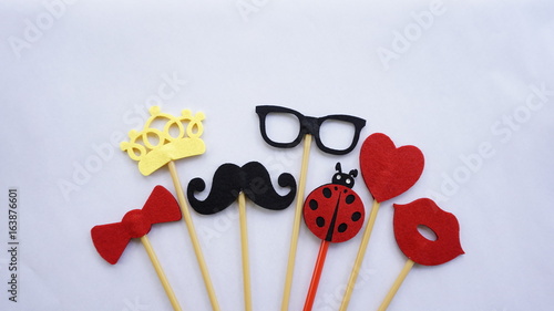Top or flat lay view of Photo booth props a black mustache a black glases, a red bow tie, a ladybird, a red heart shape, a red lips and a yellow crown on a white isolated background flat lay. Birthday