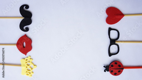 Top or flat lay view of Photo booth props a black mustache a black glases, a ladybird, a red heart shape, a red lips and a yellow crown on a white isolated background flat lay. Birthday parties and we