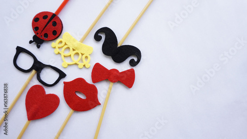 Top or flat lay view of Photo booth props a black mustache a black glases, a red bow tie, a ladybird, a red heart shape, a red lips and a yellow crown on a white isolated background flat lay. Birthday