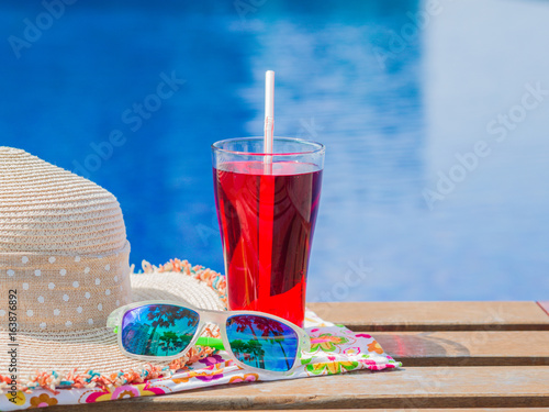 sungrasses, hat, rolled up towels and red soft drink with at the side of swimming pool. Vacation, beach, summer travel concept