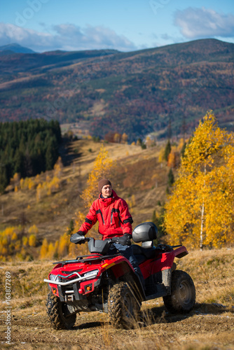 Man on quad bike in the mountains on a blurred background mighty mountains and forests in the autumn sunny day
