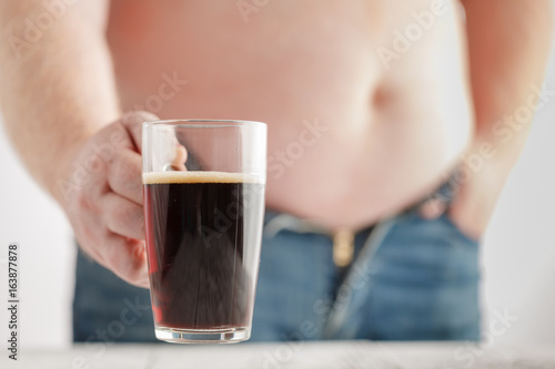 Caucasian man with Fat Beer Belly, holding a glass of dark ale. Jeans are very tight