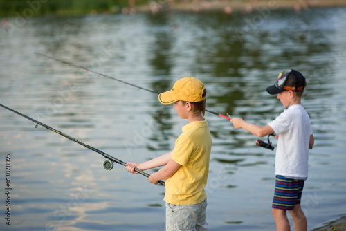 Two boys are fishing on the beach at sunset
