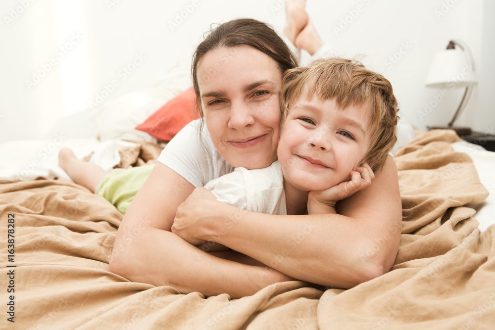 mother with her little son relaxing and playing in the bed at the weekend together, lazy morning. 