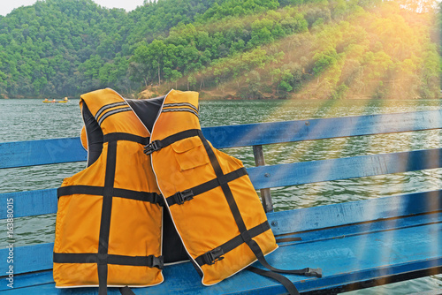 Yellow-orange lifejacket on a ship against the backdrop of the coastline. In the sun.