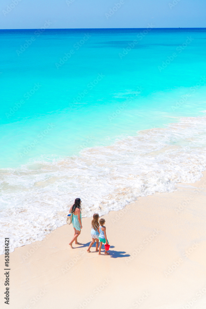 Adorable little girls and young mother on white beach. View to the family and ocean from above Adorable little girls and young mother on white beach. View to the family and ocean from above