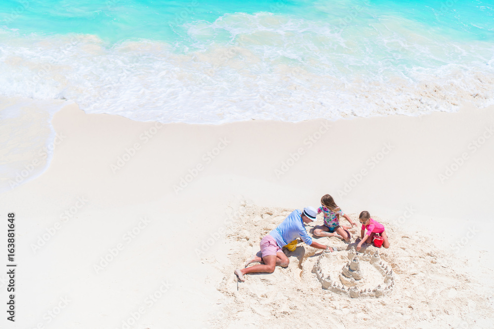 Father and little daughters making sand castle at tropical beach Father and little daughters making sand castle at tropical beach