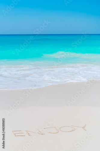 Word Enjoy handwritten on sandy beach with turquoise water