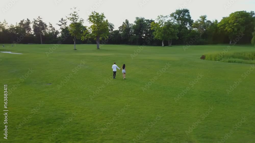 Aerial View Of Young Couple Walking In Summer Park, Circling Drone Shooting Man And Woman Outdoors Aerial View Of Young Couple Walking In Summer Park, Circling Drone Shooting Man And Woman Outdoors