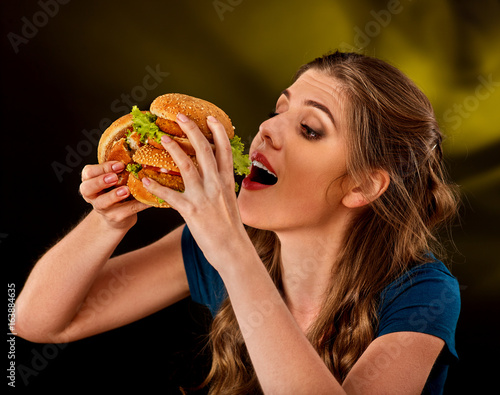 Woman eating hamburger. Student consume fast food on table. Cook teaches to cook and shares recipes. Girl eagerly eats junk alone without embarrassment. Delivery of food at home.