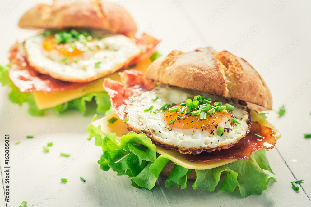 Fresh burger with lettuce, bacon and eggs on white table