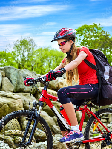 Woman on bicycle ride mountain. Girl traveling in summer park. Early morning with blue sky and clouds. Cycling person with rucksack. Female loves extreme sports.
