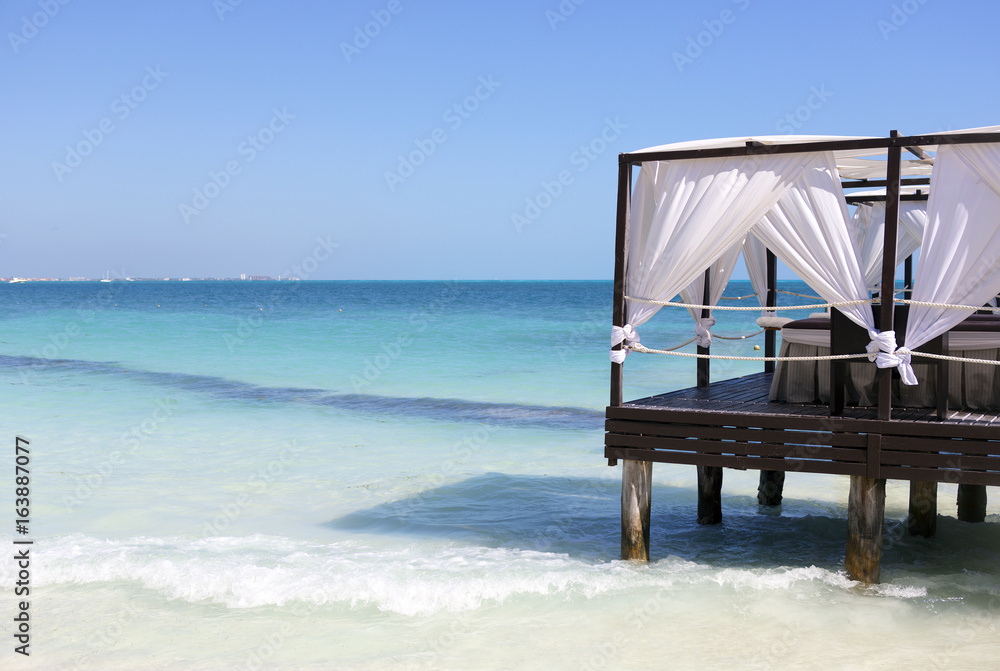 Luxury place for vacation. Massage beds on the beach. White curtains and turquoise water.