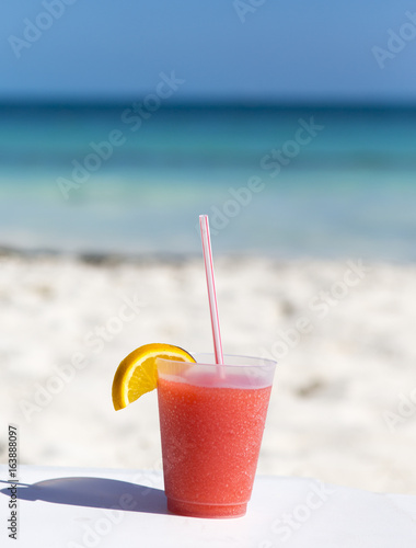 Fresh cocktail with a straw against the turquoise waters. White sand beach with isolated drink.