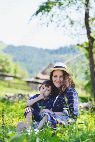 A woman with a baby is sitting on the grass in the mountains.